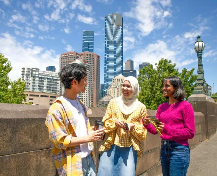 3 young people stand outside in Melbourne CBD, chatting to one another and smiling.